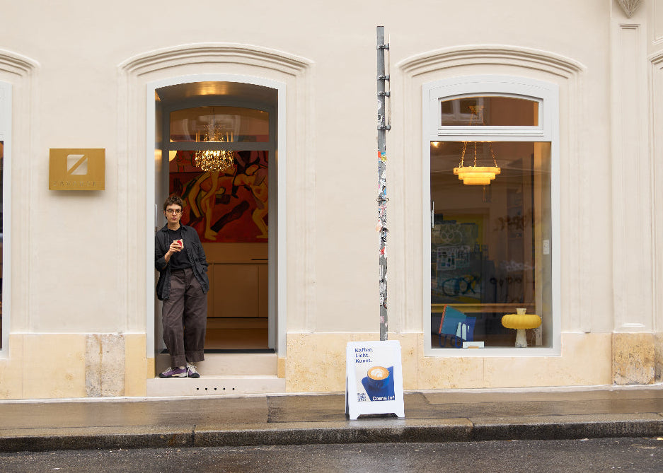Person taking a photo of a store front with a sign on the sidewalk.